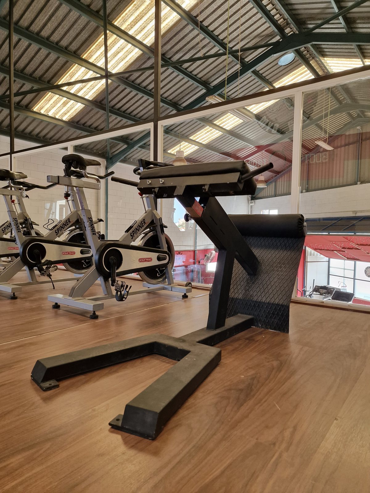 Interior del gimnasio Olimpo NGR Gym con una máquina de hiperextensiones en primer plano y bicicletas estáticas al fondo.